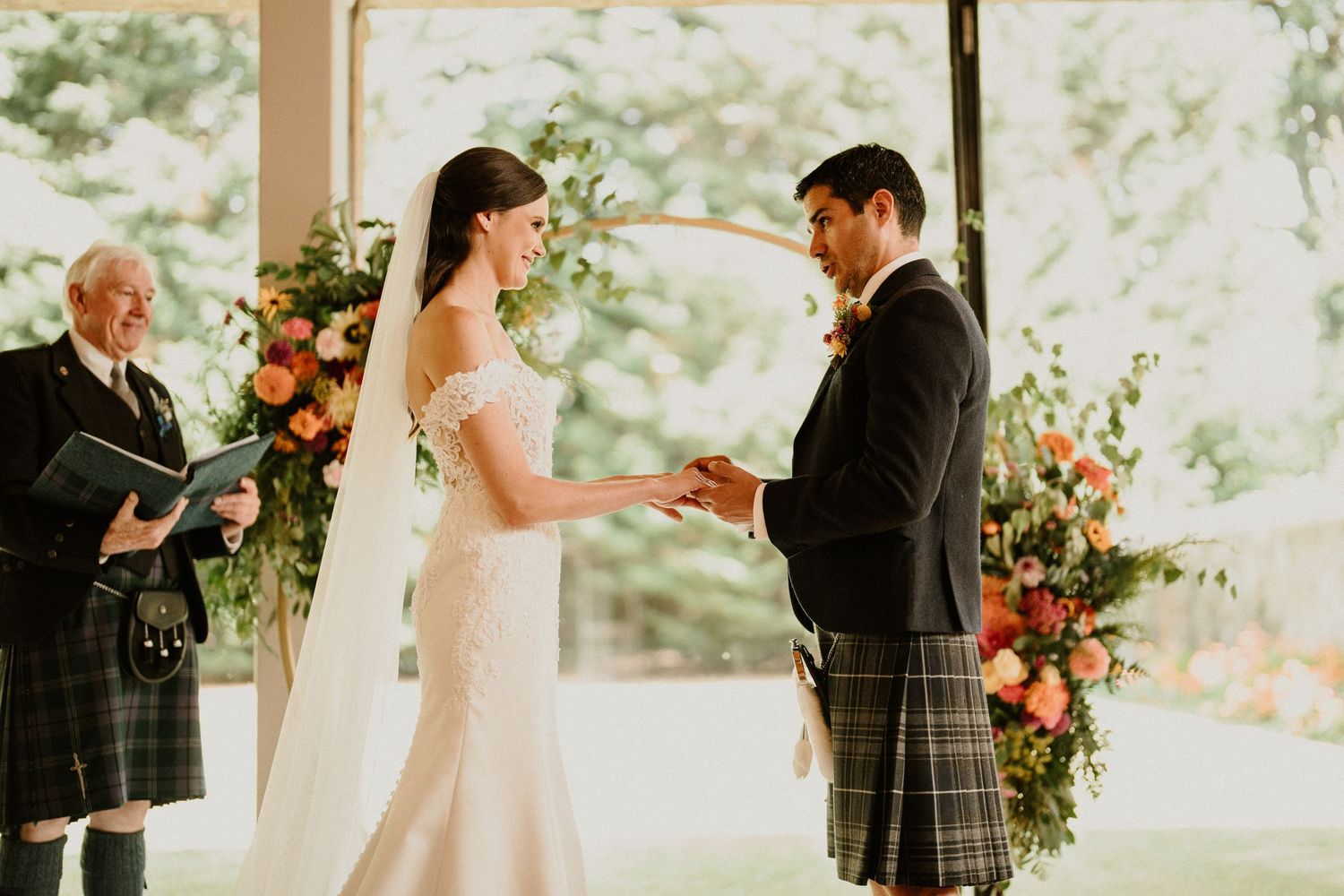 Wedding ceremony in bright sunlit room with floral arch and natural decor.