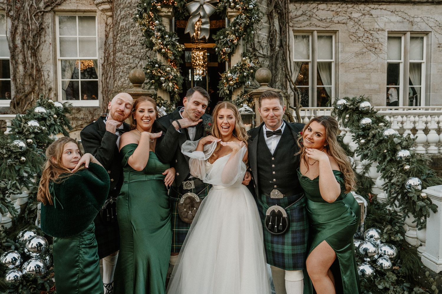 Wedding party in green dresses and kilts pose together at castle entrance.