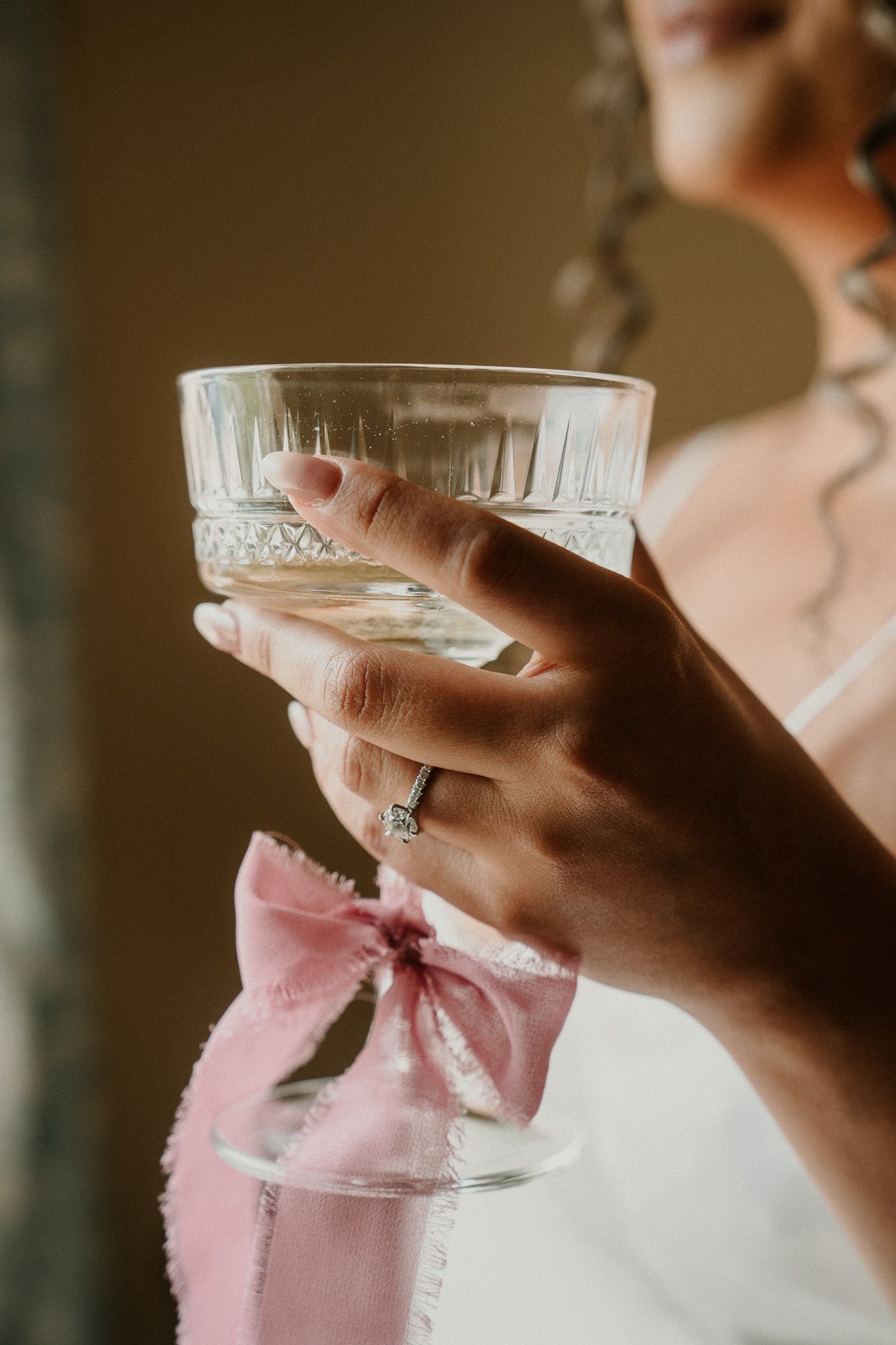 Hands holding vintage champagne coupes in soft pink lighting.