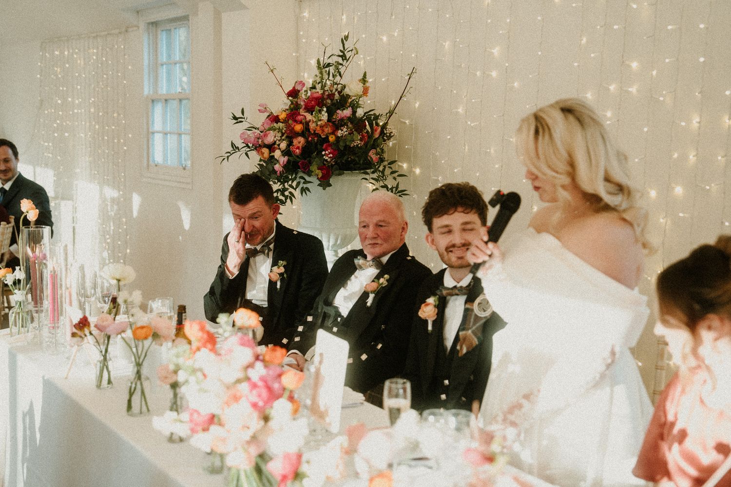 Wedding celebration with guests seated at long tables decorated with pink floral arrangements.