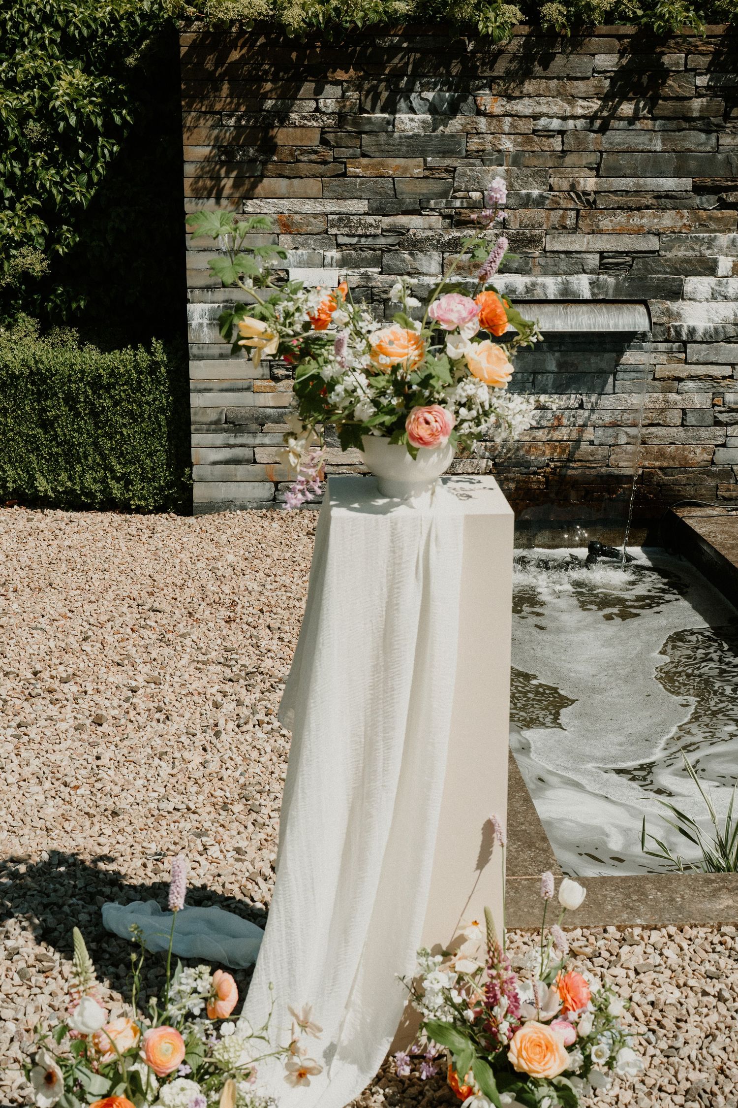Elegant floral arrangements with peach roses and white flowers against a rustic stone wall.