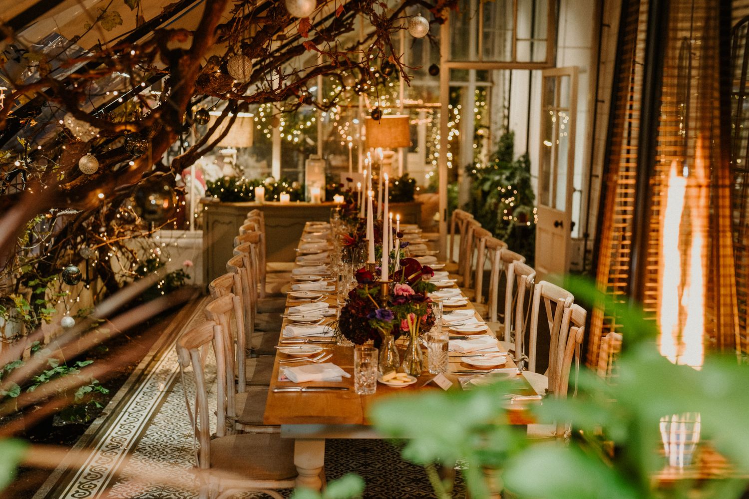 Intimate dinner setting with white chairs and glowing candles under branches decorated with fairy lights.