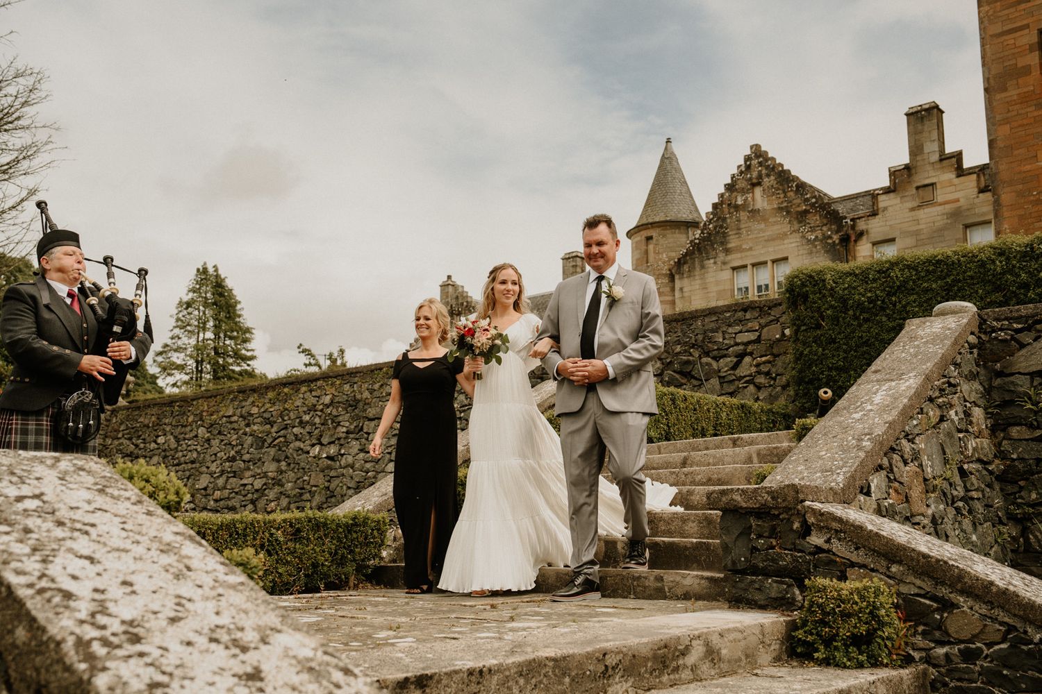 Wedding party walking up stone steps at historic castle venue with rustic architecture.