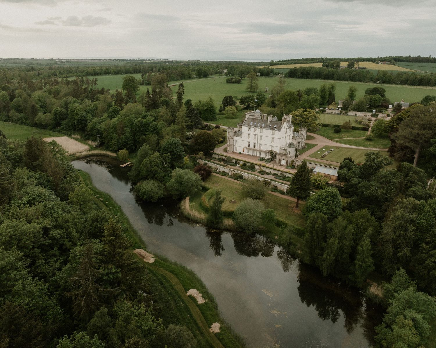 Aerial view of a grand white château surrounded by lush greenery and a winding river in the French countryside.