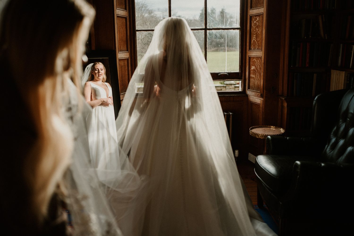 Wedding dress silhouetted against window light in elegant getting ready room.