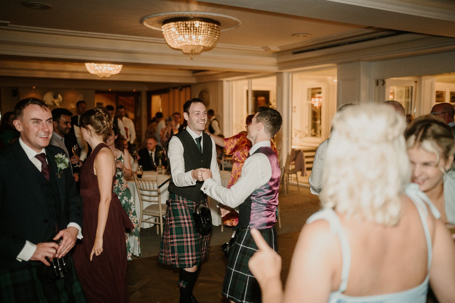 Wedding reception guests dance and celebrate in an elegant ballroom with crystal chandeliers.