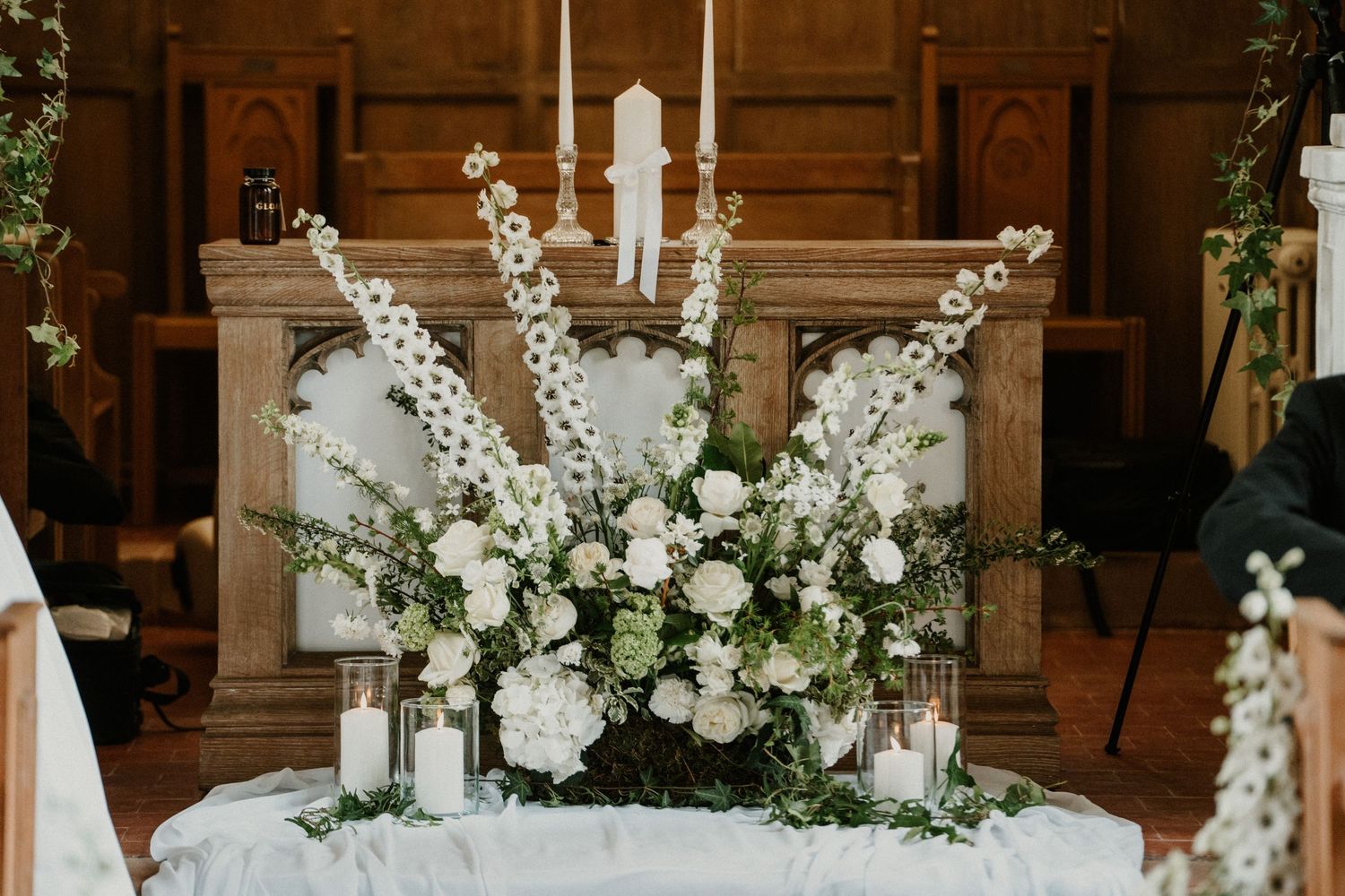 Elegant white floral arrangement with candles decorates a church altar table.