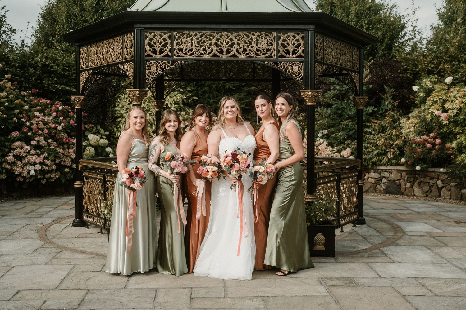 Wedding party posing together under a decorative outdoor pavilion.
