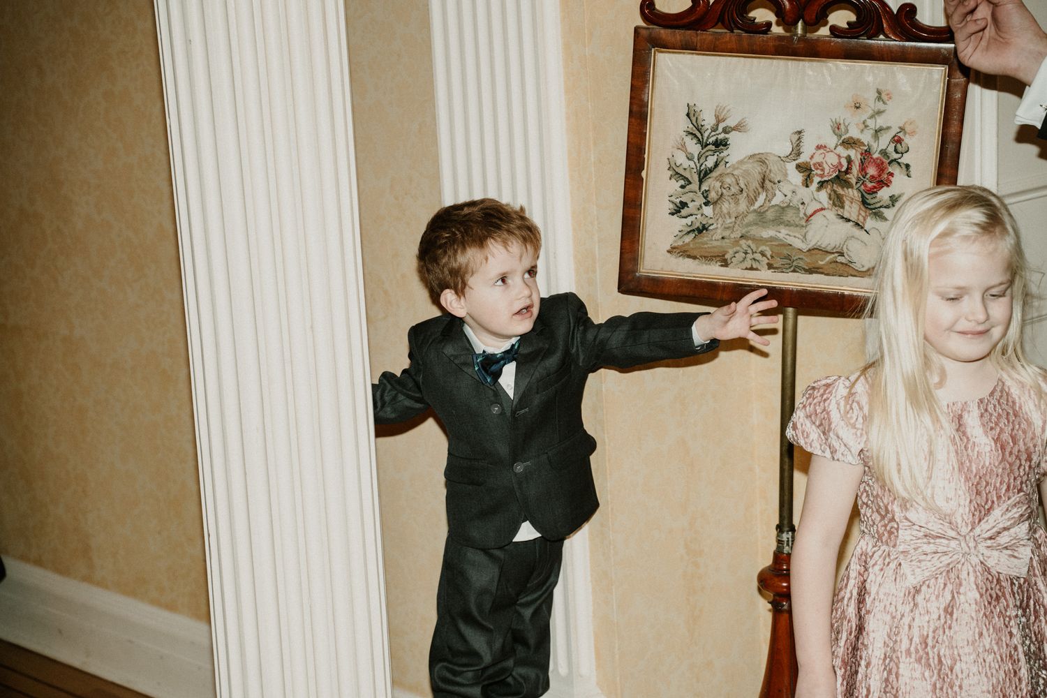 Two young children in formal attire play and pose during a wedding celebration.