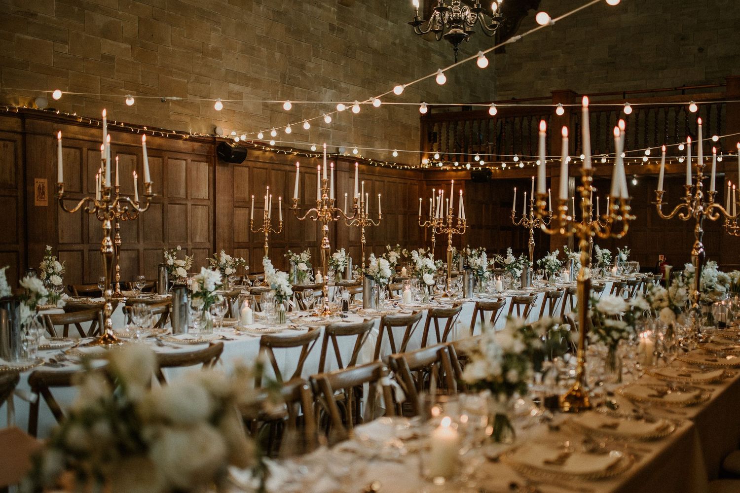 String lights and candles illuminate an elegant wedding reception setup with long dining tables.