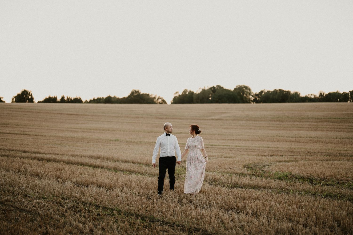 A couple shares an intimate moment in a rural wheat field during sunset.