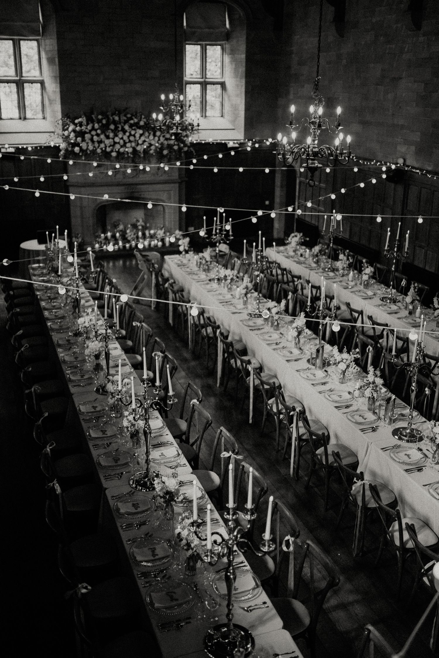 Black and white aerial view of elegant banquet hall with long tables, candelabras, string lights, and floral decor.