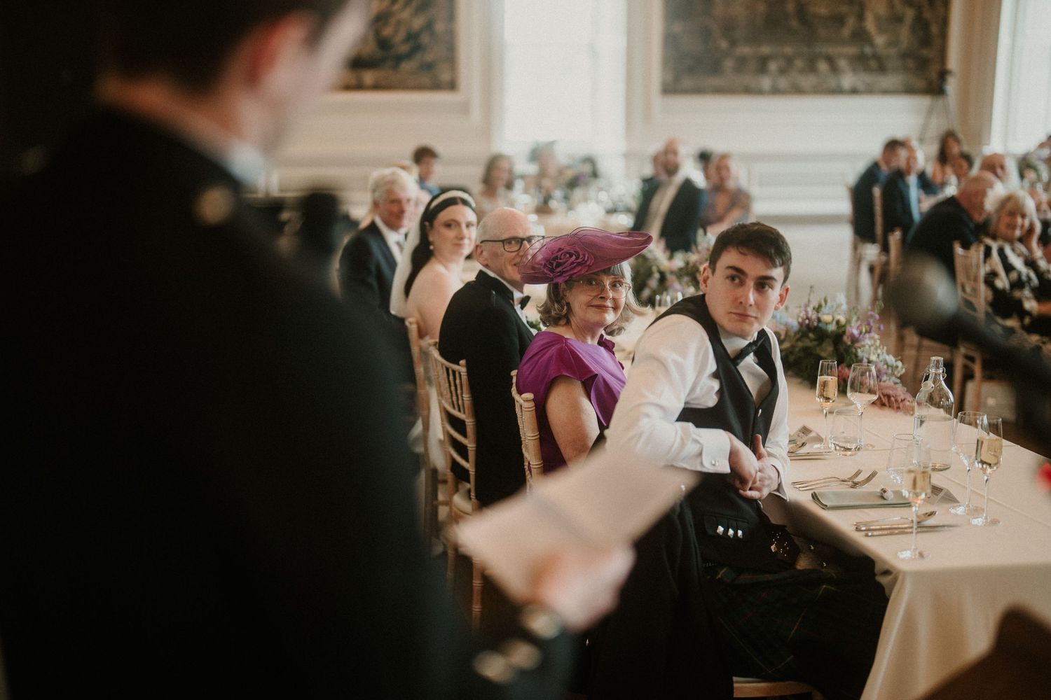 Wedding reception guests enjoying dinner at round tables in an elegant white room.