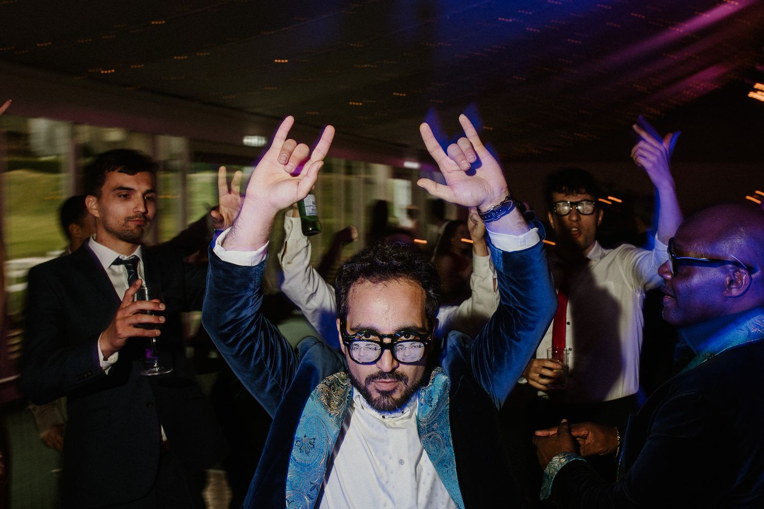 Wedding guests raising their hands in celebration on a dark dance floor with purple lighting.