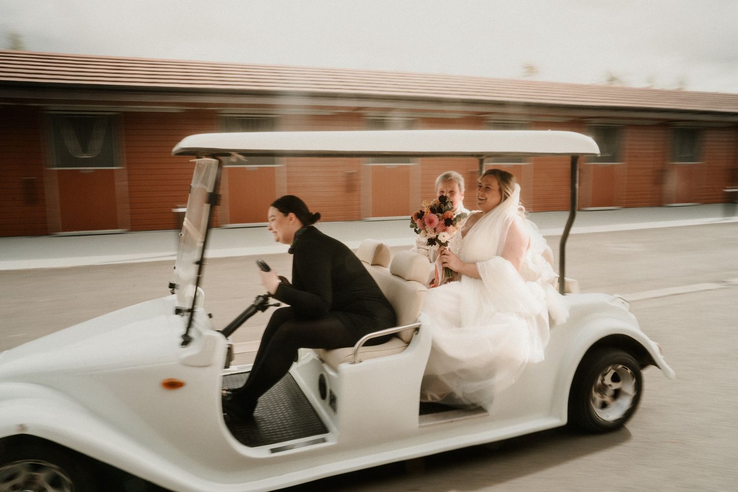 White vintage car carries wedding party members along venue driveway.