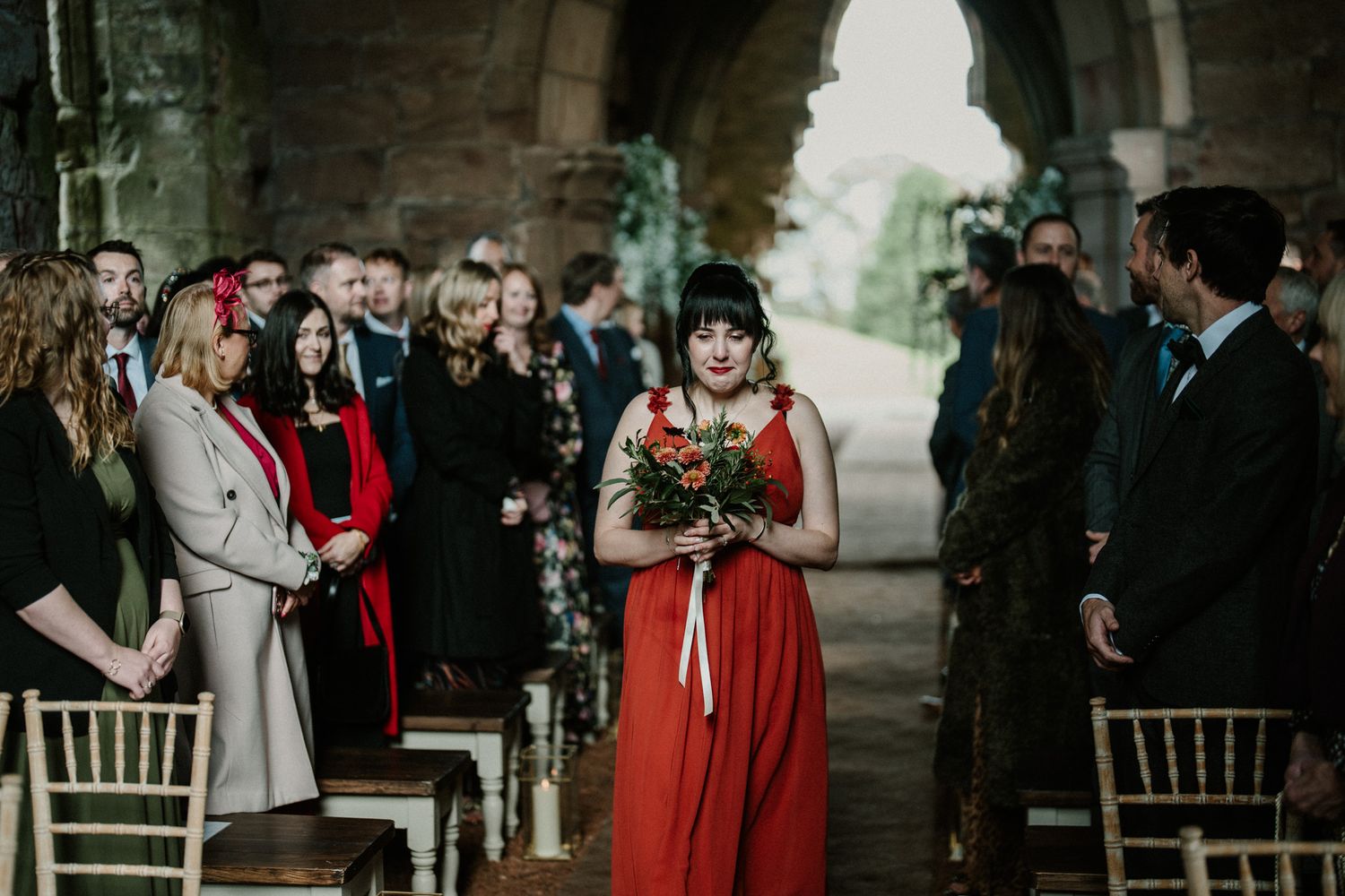 Wedding attendees fill stone church interior decorated with floral arrangements.