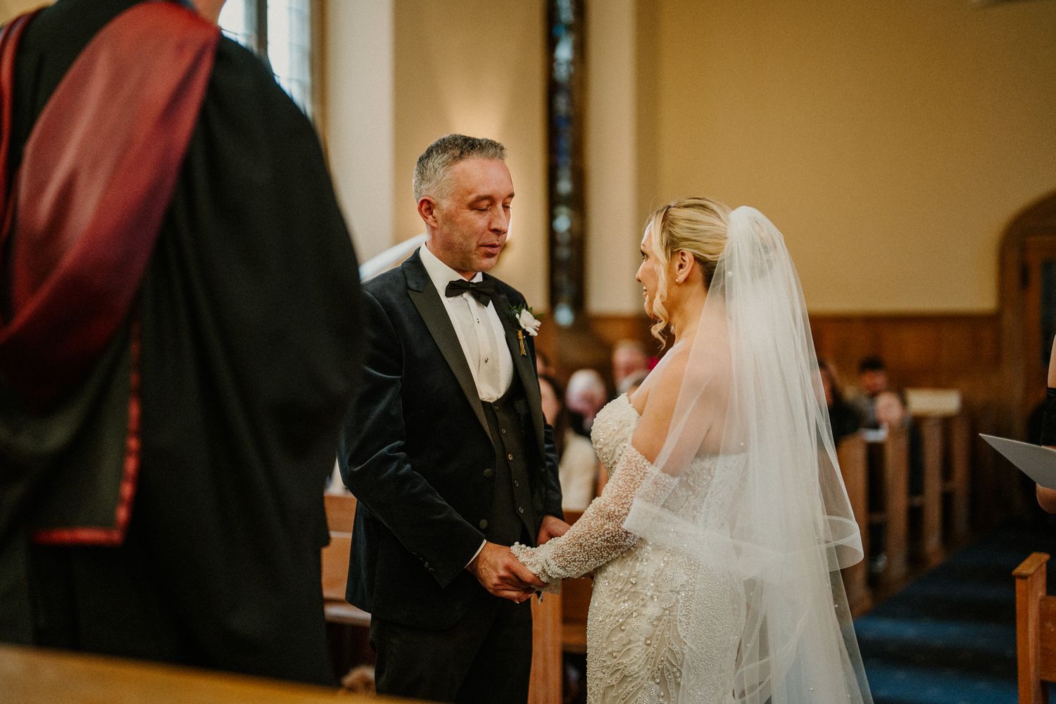 A wedding ceremony takes place in a traditional church with warm lighting and wooden pews.