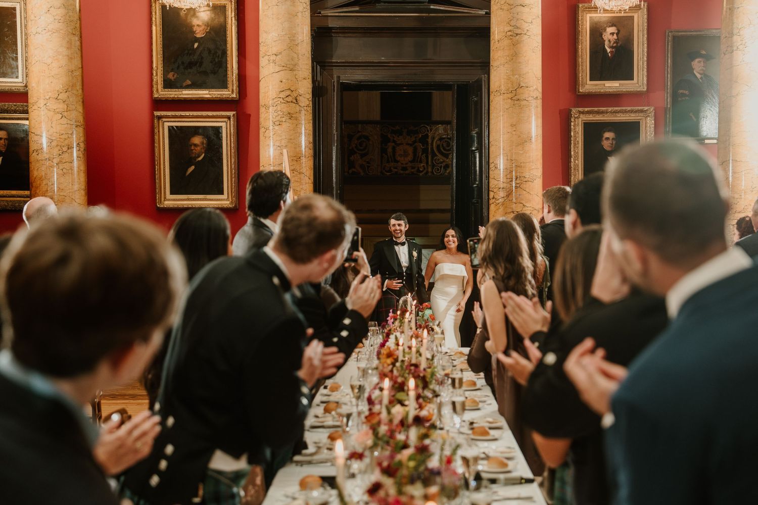Elegant wedding reception in a historic red-walled dining room with ornate portraits and chandeliers.