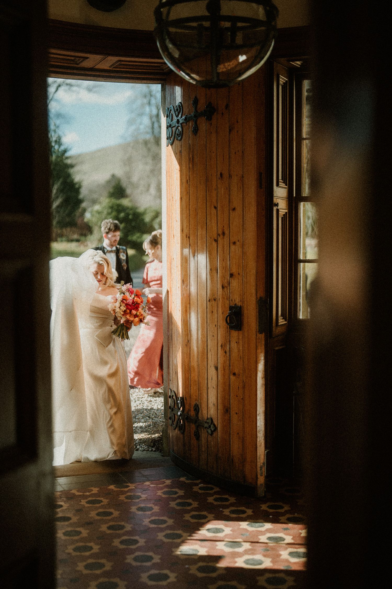 Glimpse through wooden doorway of wedding party gathering outside rustic venue.