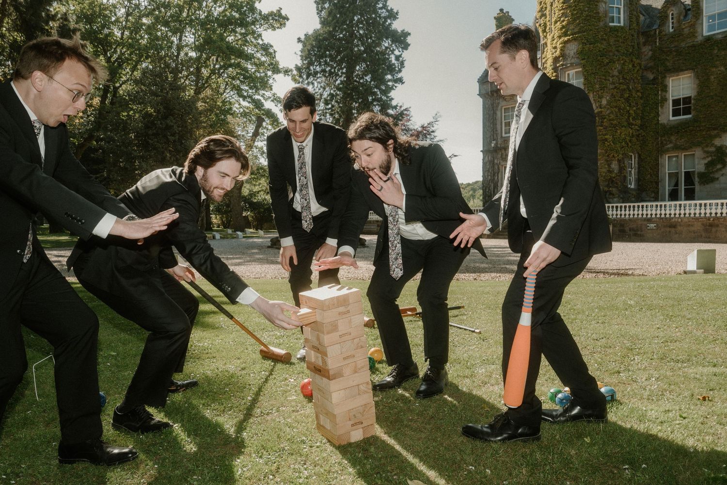 Groomsmen participate in lawn games during wedding day festivities at historic venue.