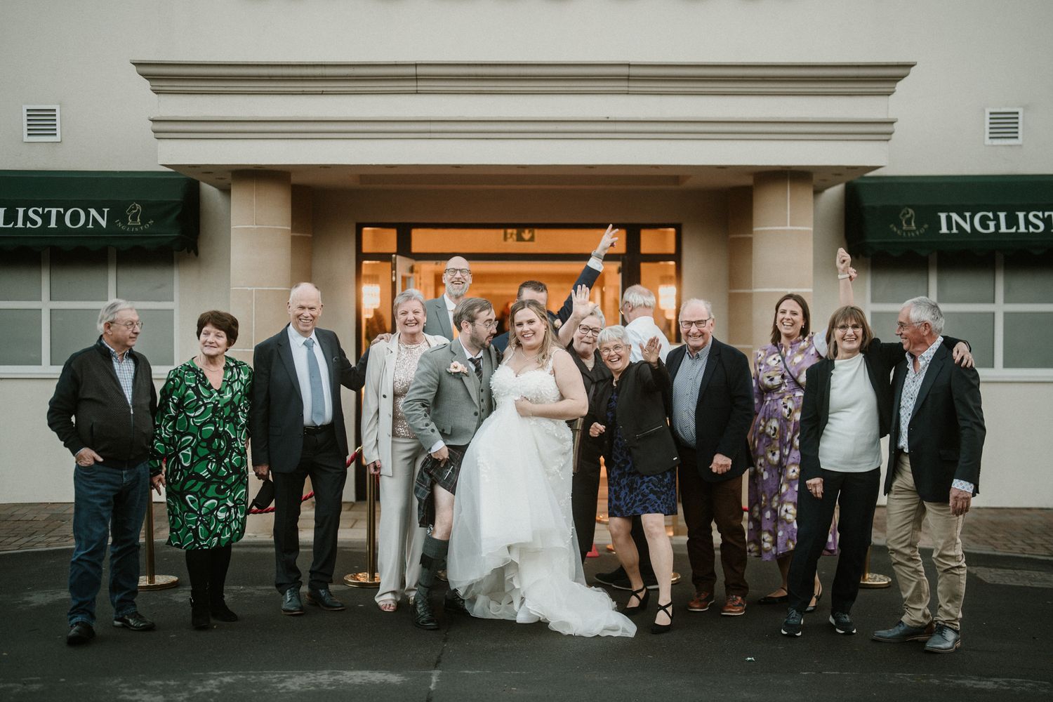Wedding guests line up outside a building with traditional architecture on an overcast day.