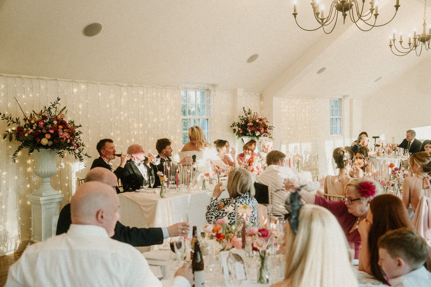 Wedding reception tables set with elegant decor and floral arrangements under crystal chandeliers.