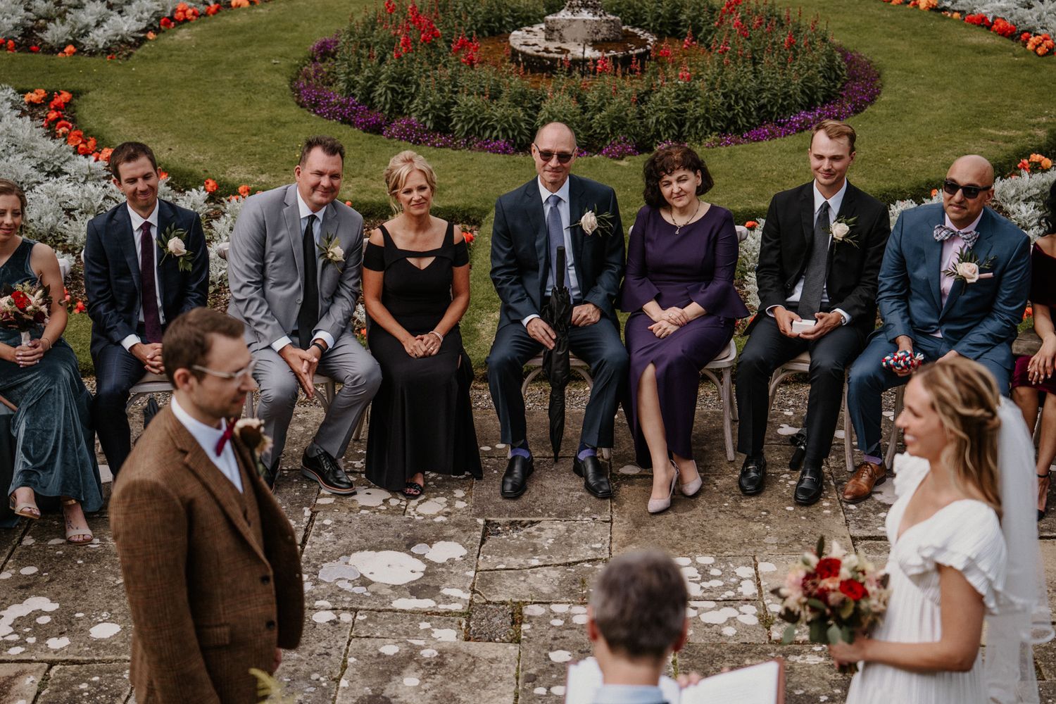 Intimate outdoor wedding ceremony on stone terrace surrounded by flowers.