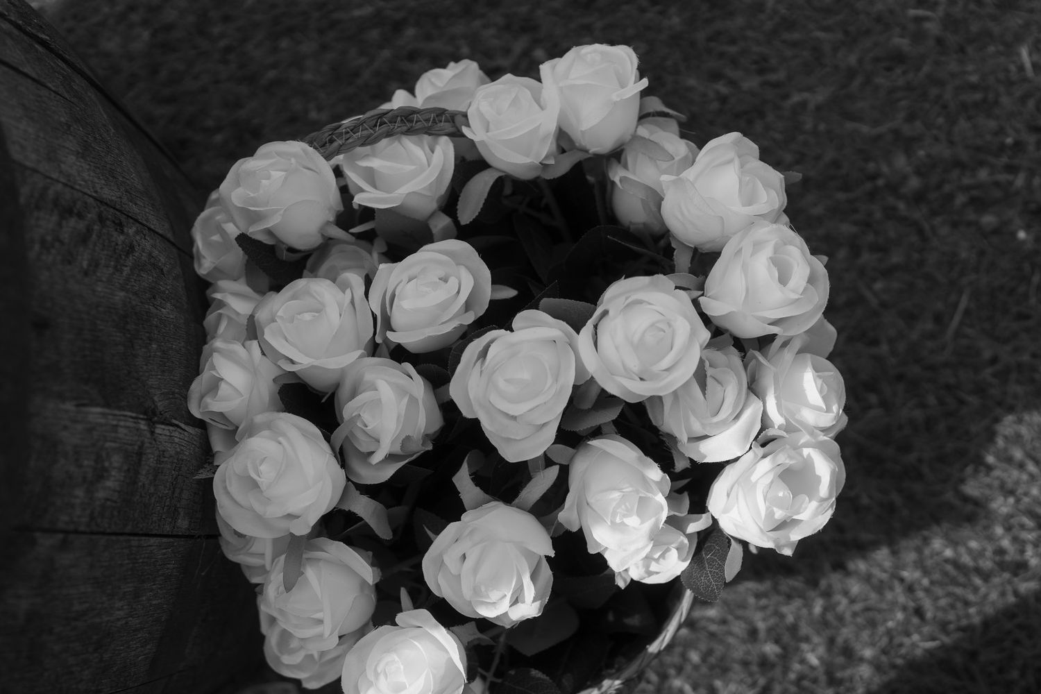 Black and white photo of a bouquet of white roses arranged in a circular pattern, viewed from above.