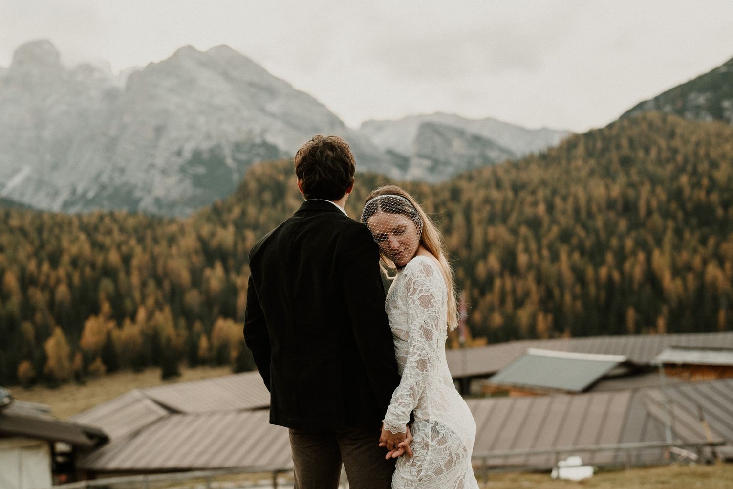 A couple shares an intimate moment against a backdrop of majestic Dolomite mountains and autumn forests.
