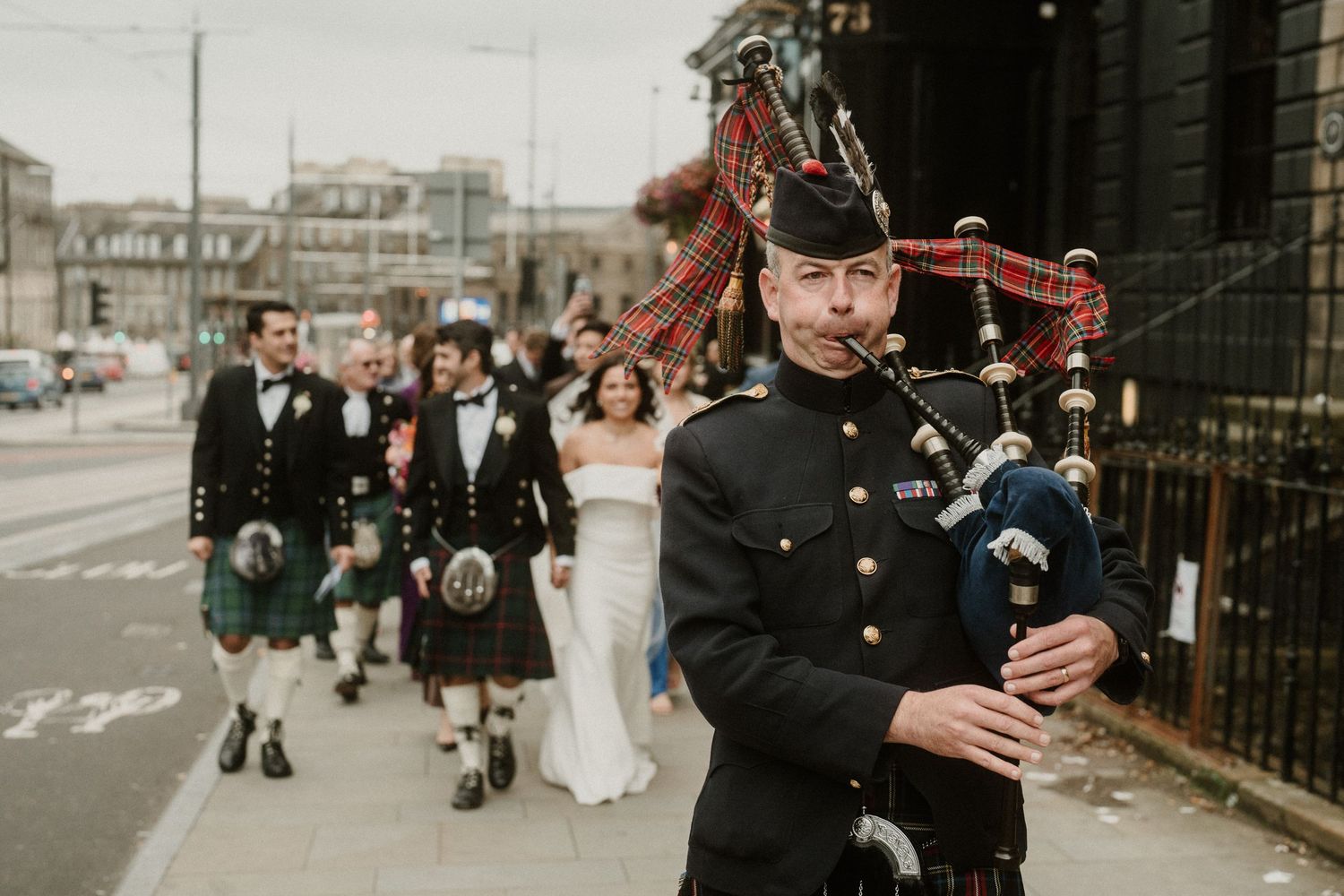 Traditional Scottish bagpiper performs during wedding procession on urban street.