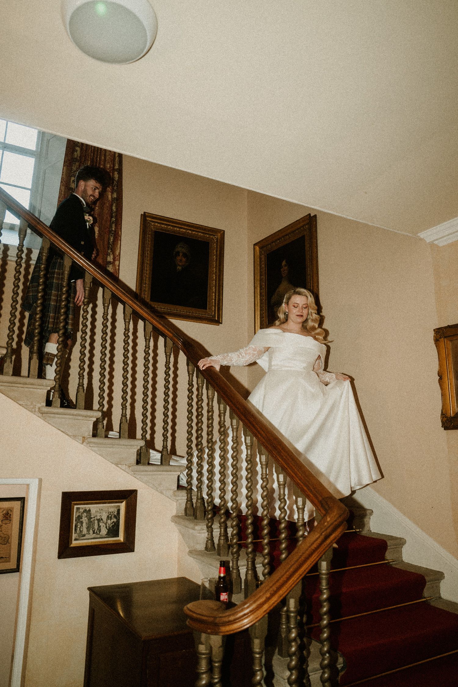 Elegant staircase scene with vintage portraits and red carpet in a historic mansion.