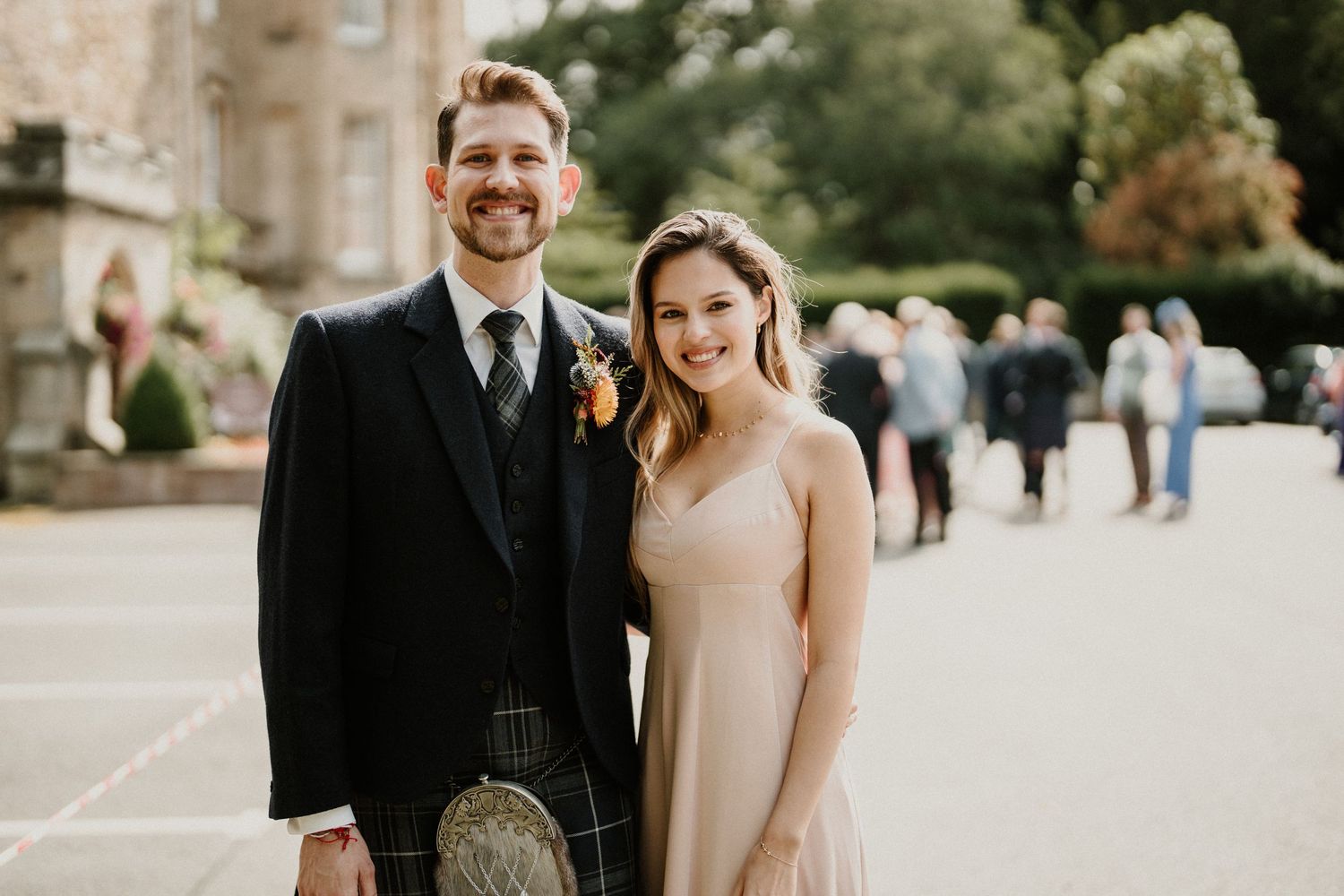 Wedding party members walk and laugh together on stone pathway outside historic building.