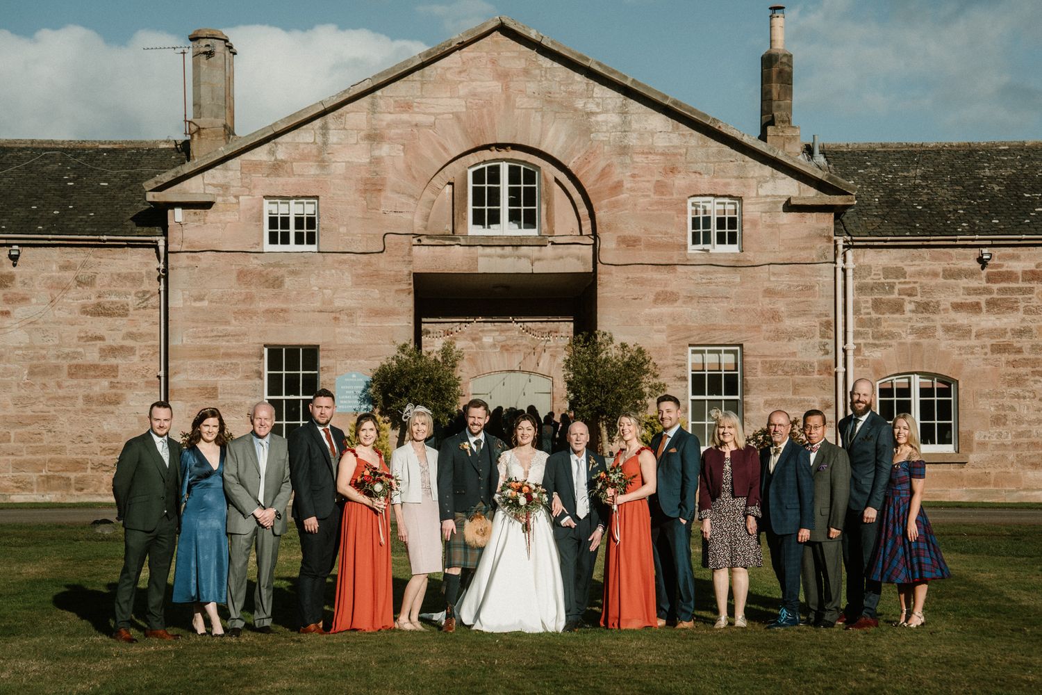 Wedding group photo of guests and wedding party in front of pink stone mansion.