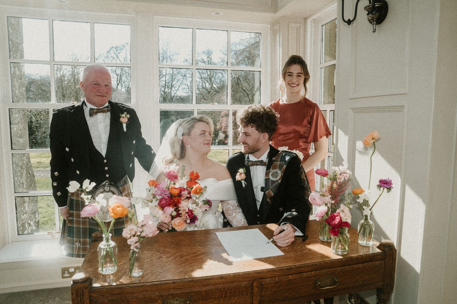 Wedding party gathered around an antique wooden table signing documents during a traditional ceremony.