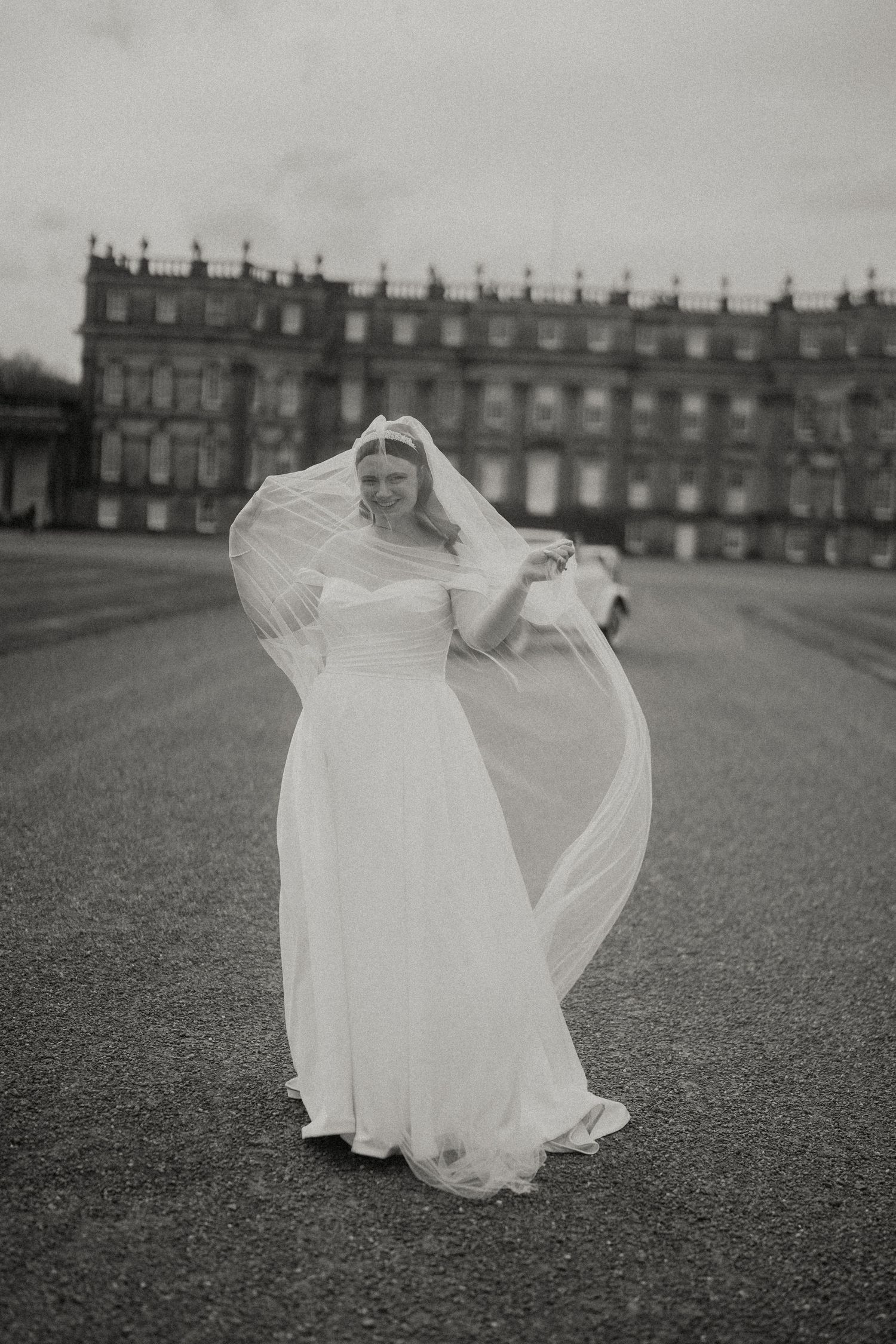 A person in a flowing white wedding dress twirls gracefully on a grand lawn in front of a historic manor house.