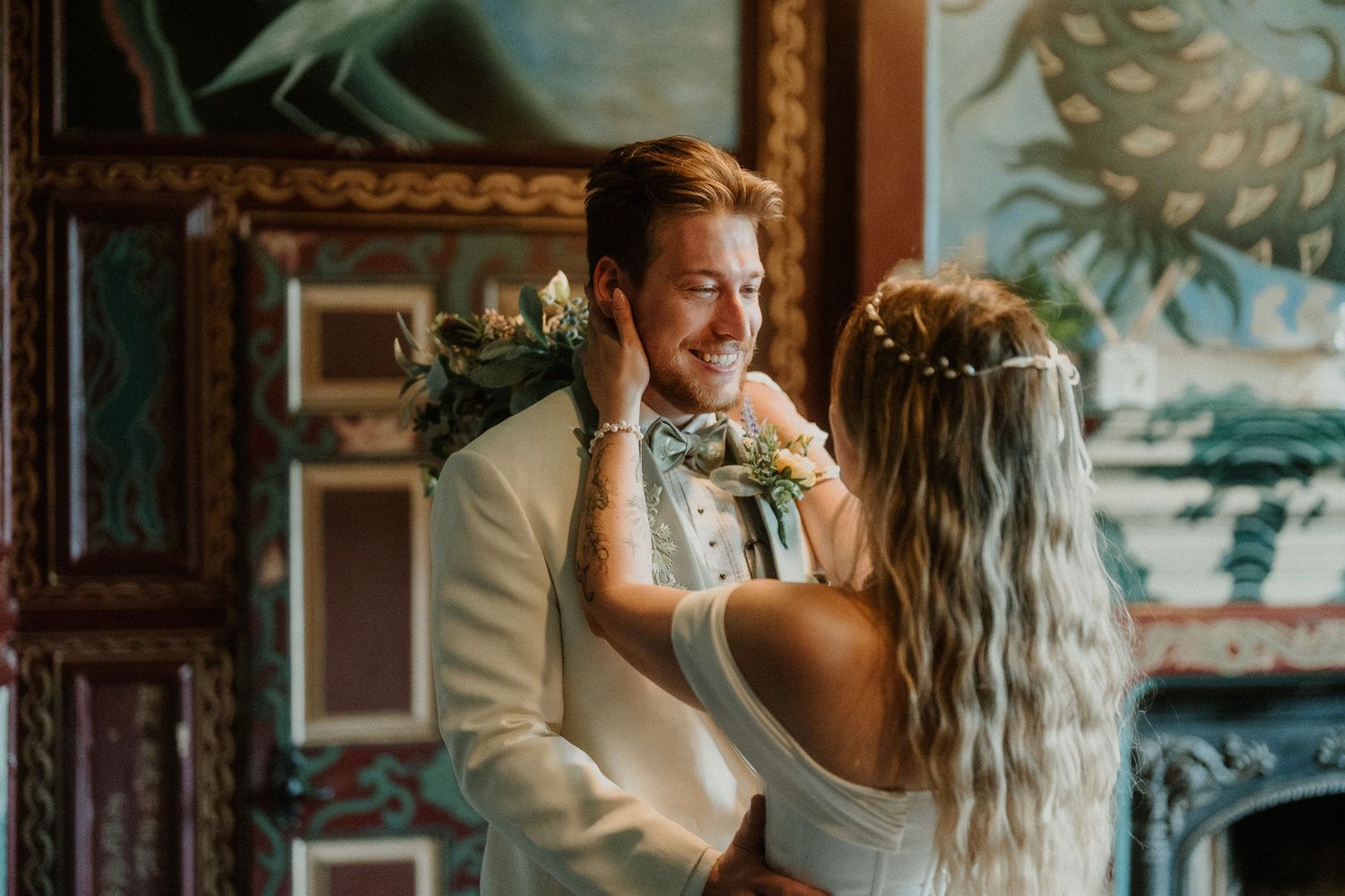 Bride adjusting groom's floral boutonniere in elegant venue, both smiling during wedding day preparations.