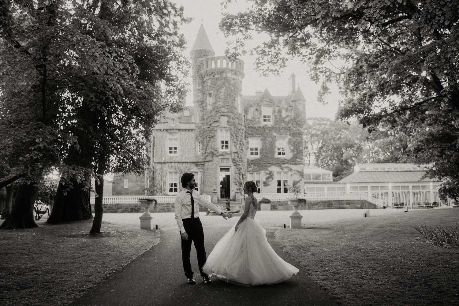 A panoramic black and white view of a couple walking near a grand castle estate.