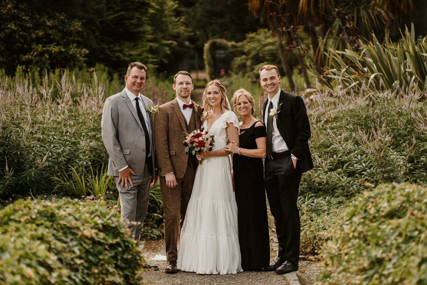A wedding party poses for a portrait on a garden path surrounded by lush vegetation.