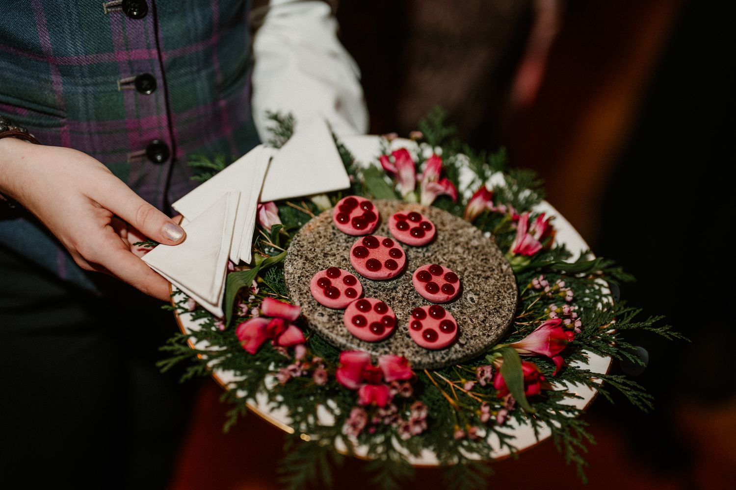 A decorative plate of red desserts garnished with greenery at a wedding reception.