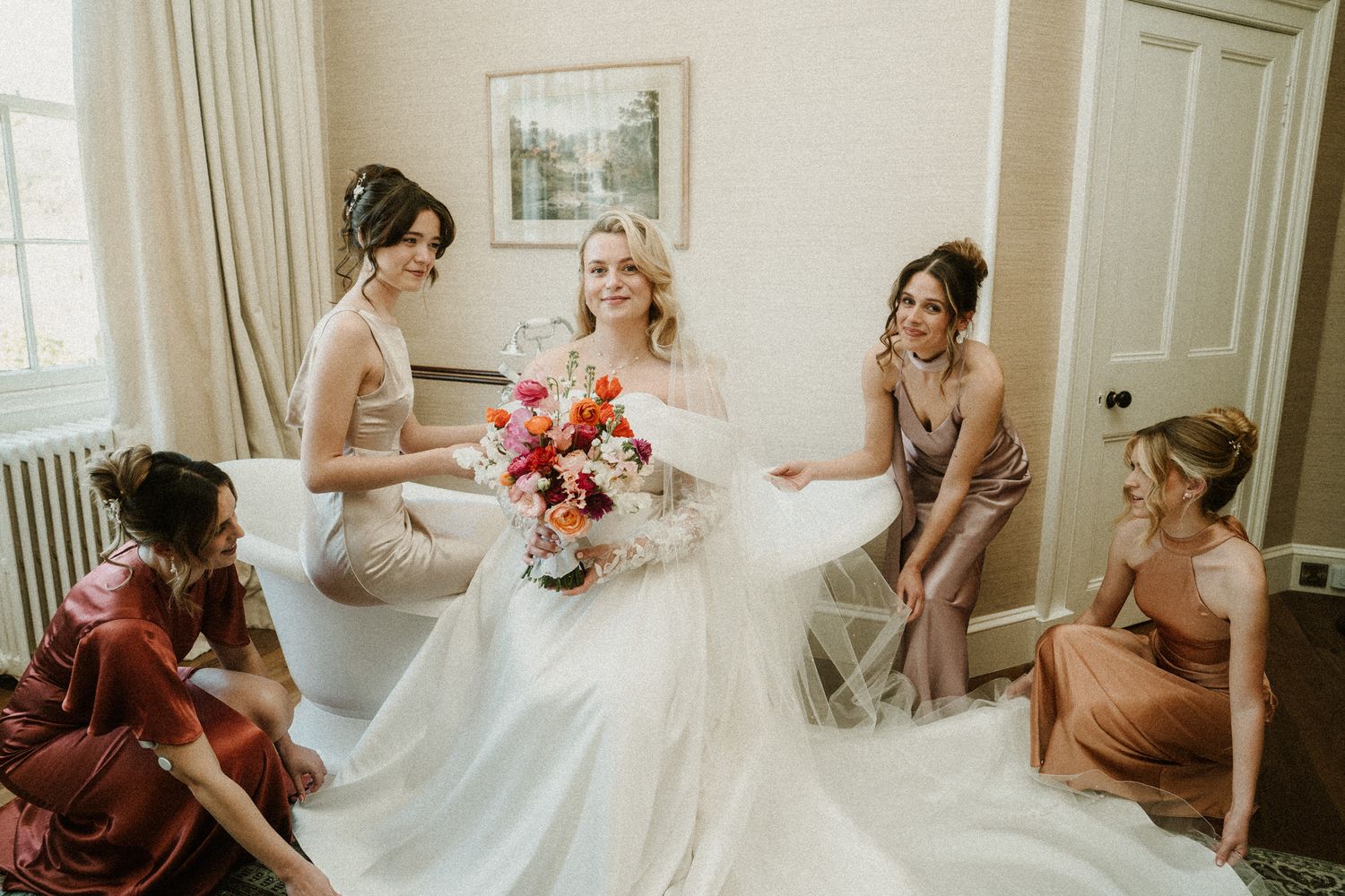 Bridesmaids in earth-toned dresses gather on a patterned rug with the bride.