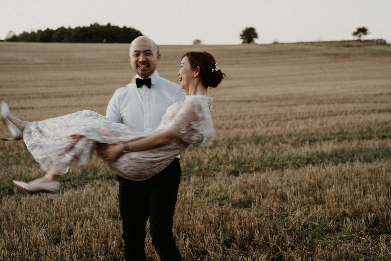 A playful couple dances and spins in a golden wheat field at dusk.