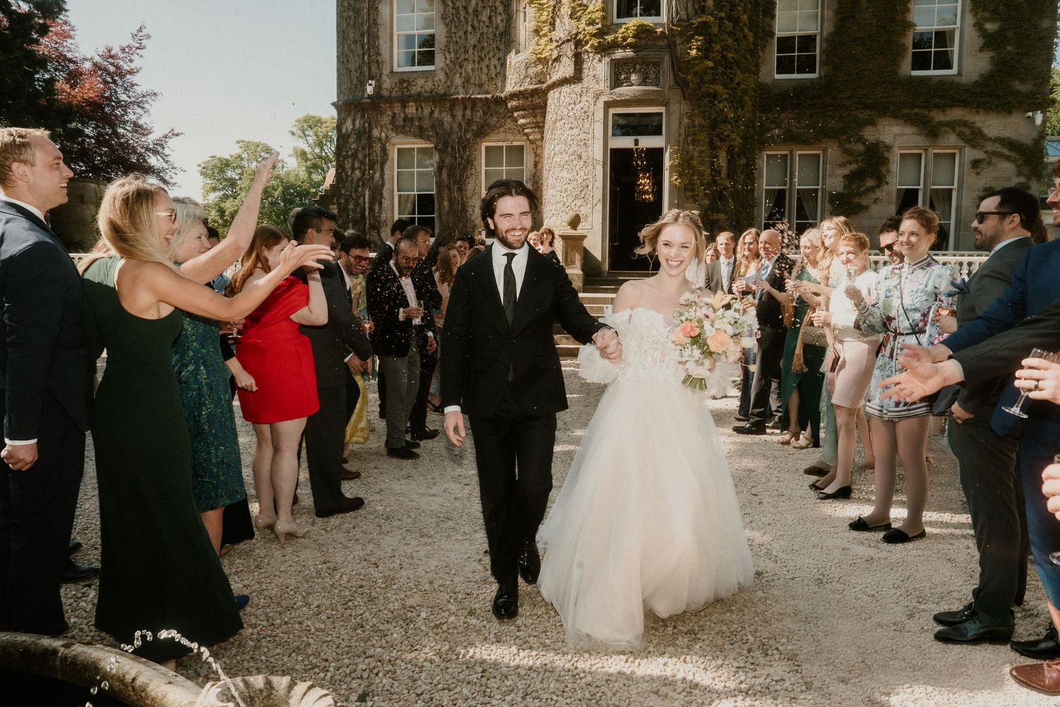 Wedding party exit with guests tossing confetti outside a grand stone building.