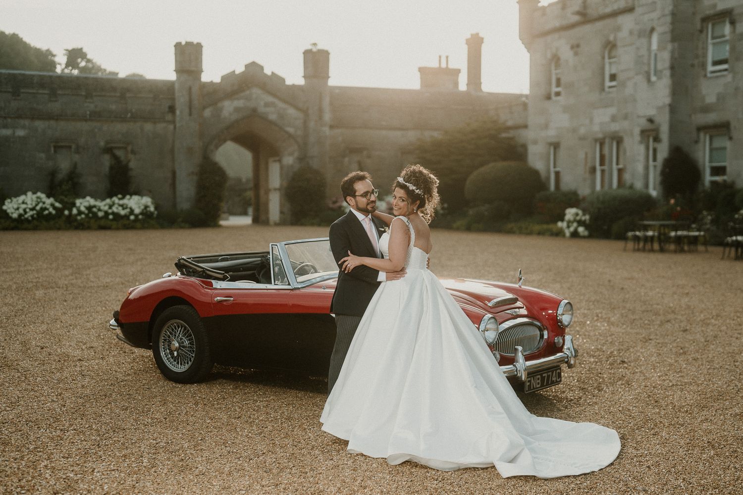 Romantic sunset wedding photos featuring a vintage red convertible car at a castle venue.