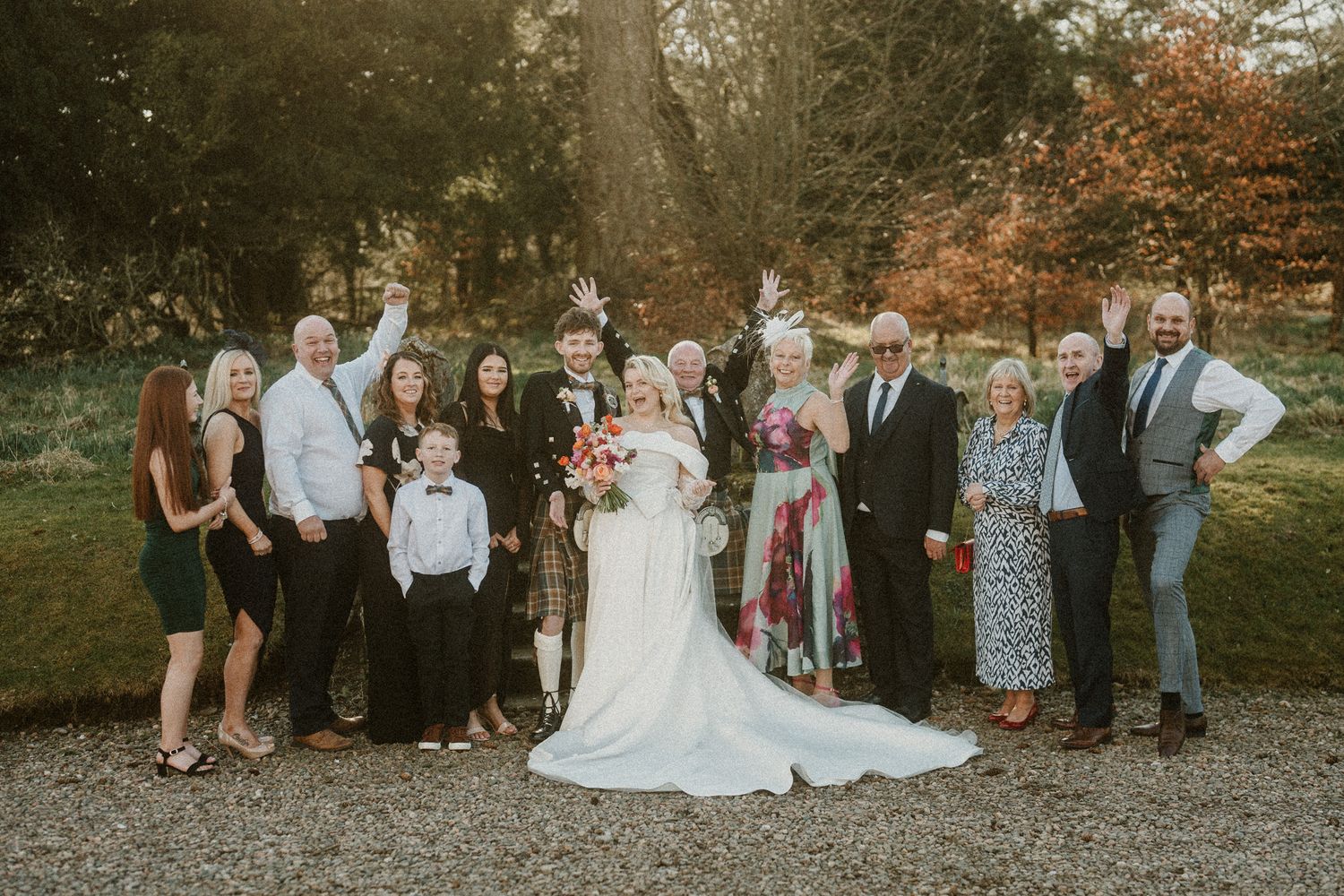 Extended wedding party gathers for group photo in casual outdoor setting during fall.