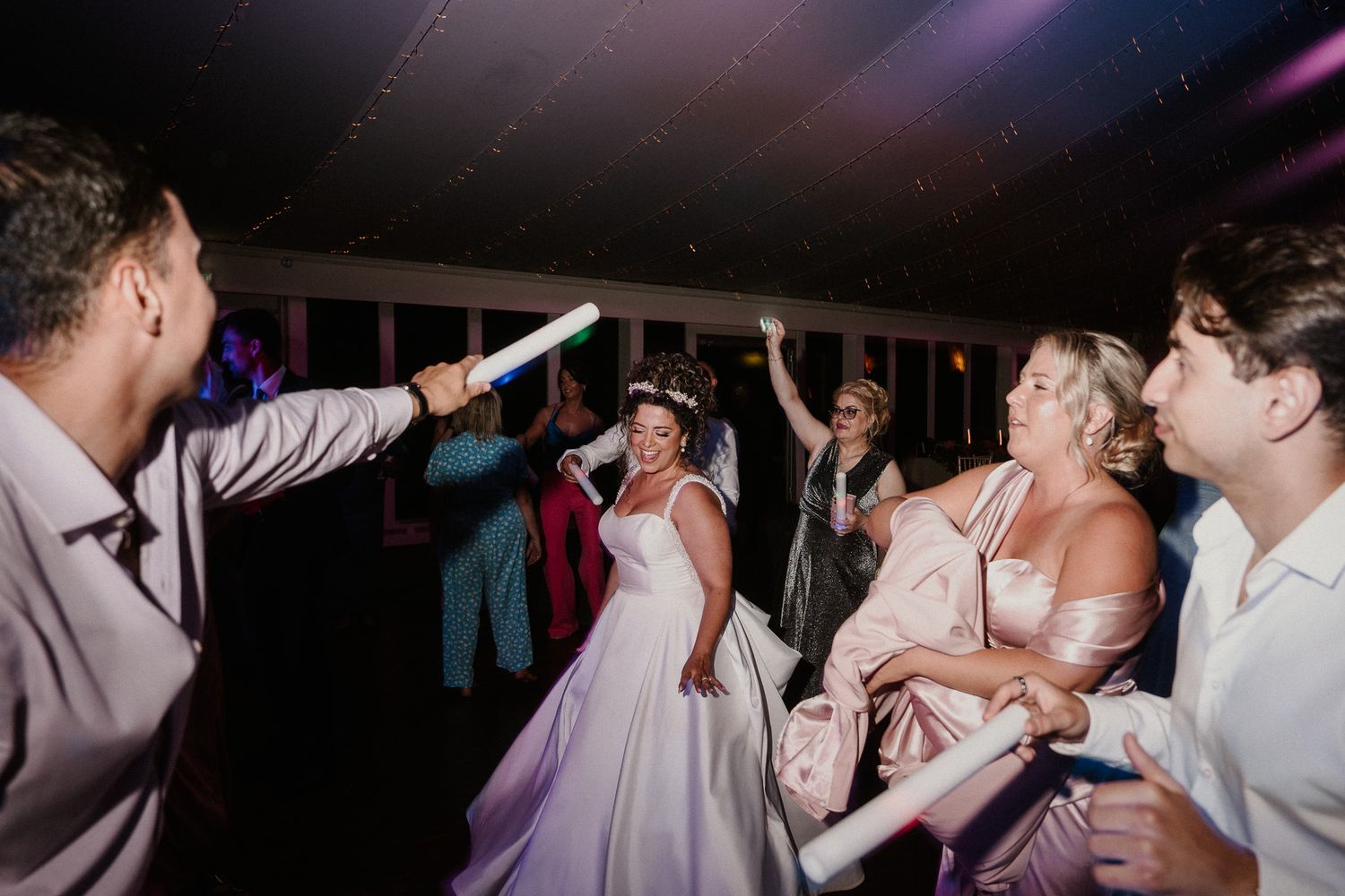 Wedding reception dance floor filled with guests celebrating under purple lighting.