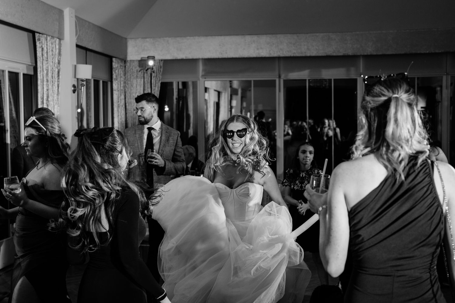 Wedding guests dancing and celebrating at an indoor reception venue in black and white.