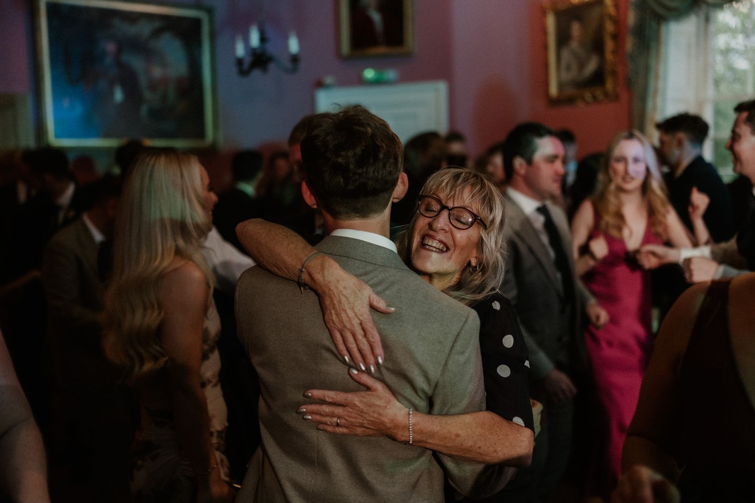 Guests embracing and laughing joyfully on a wedding dance floor in an elegant venue.