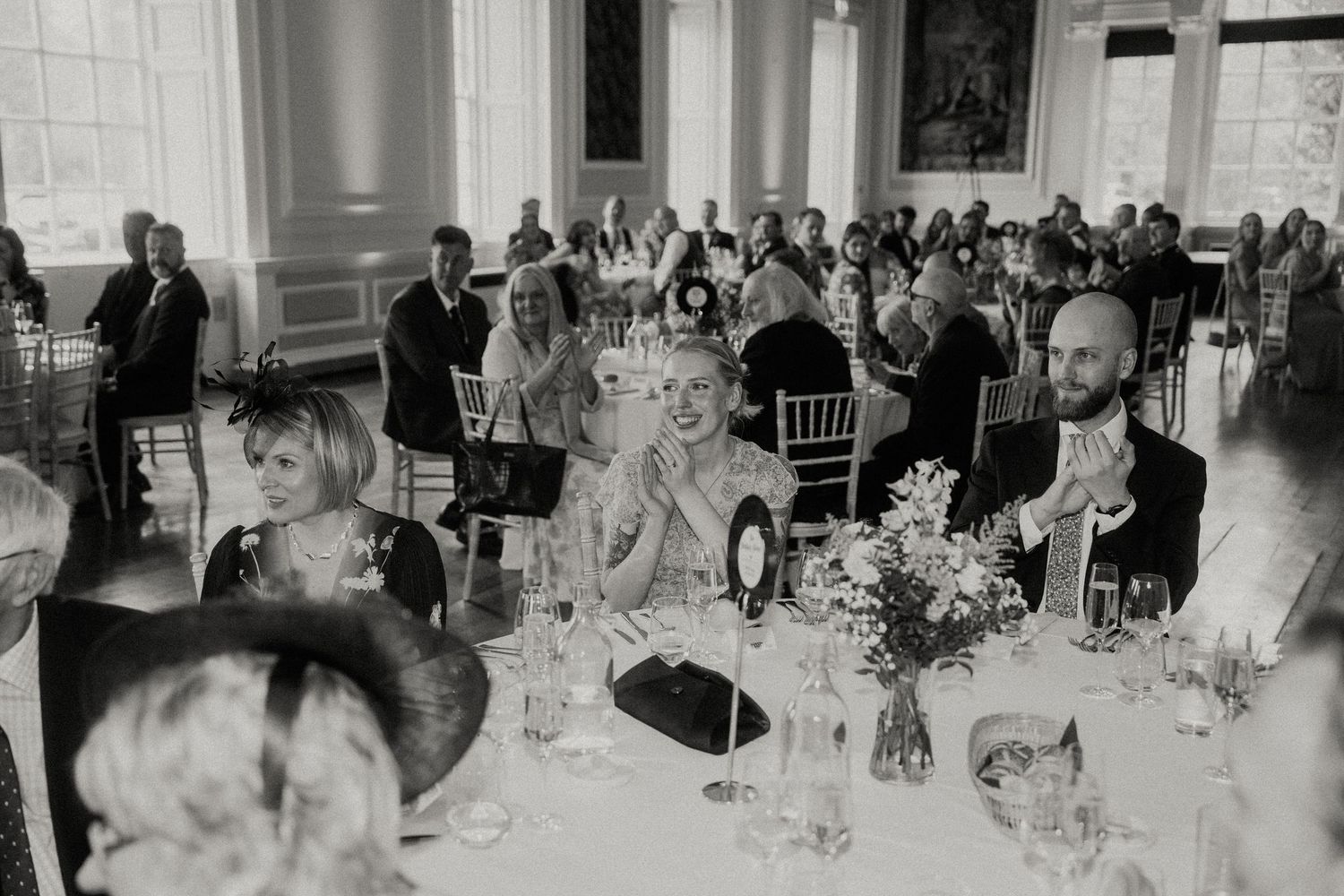 Wedding reception guests seated at elegant tables in a bright classical ballroom.