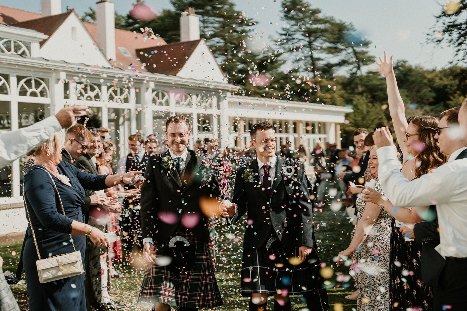 Wedding guests throw confetti as the newlyweds celebrate outside a white gazebo.