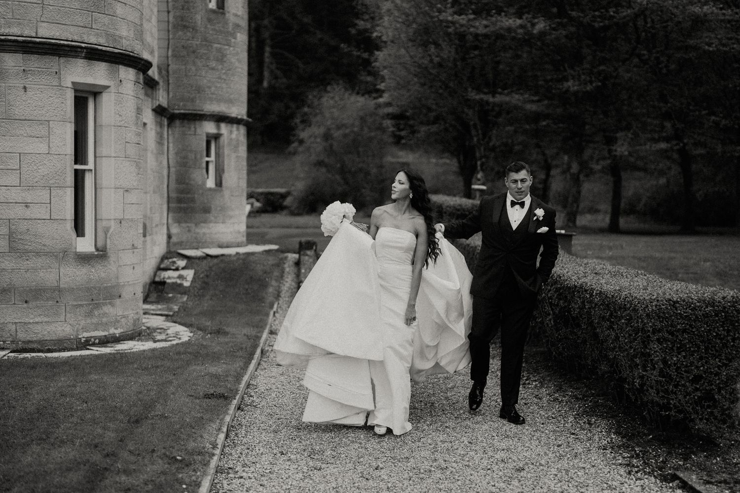 A black and white wedding photo showing a couple walking along a castle path.